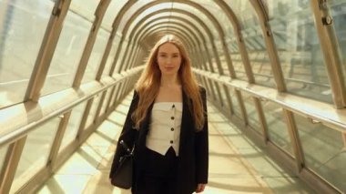 İş elbisesi içindeki genç bir kadının portresi ve havaalanının koridorunda güvenle yürüyen bir çanta ile uçuştan önce uçağa biniyor, kameraya bakıyor ve gülümsüyor.