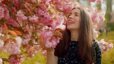 Kiraz çiçeklerini koklayan, gülümseyen, sakura ağacının altında ağır çekimde yakalanan mutlu genç bir kadının yakın plan portresi.