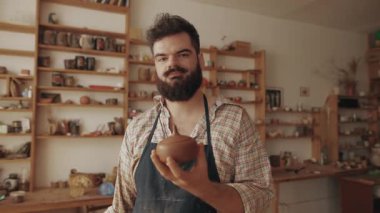  A bearded stylish potter demonstrates his finished product, a pot made of clay, in his workshop, display of completed work, master class, achievement, result of work, handmade. High quality 4k footage