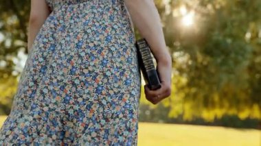 Kadınların elinde İncil 'in yavaş çekimleri altın çayır boyunca yürürken, sinematik çekim, yumuşak güneş ışığı, duygusal sahne, ruhani sembolizm, rüya gibi yaz manzarası