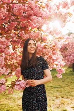 Baharda açık havada duran genç bir kadın, çiçek açmış sakura ile dikey portre, yan tarafa büyülenmiş görünüyor, rüya gibi ve romantik bir ifade, doğal güzellik.