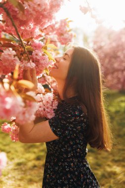 Sakura çiçeği kokan genç bir kadının dikey portresi. Gözleri kapalı, huzurlu ve rüya gibi bir bahar anı. Çiçeklerle çevrili doğal bir güzellik..