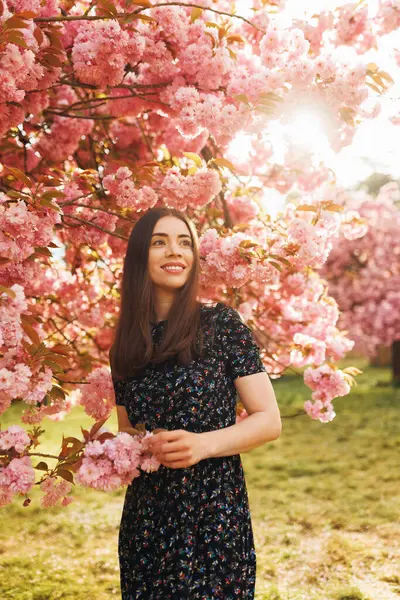 Baharda açık havada duran genç bir kadın, çiçek açmış sakura ile dikey portre, yan tarafa büyülenmiş görünüyor, rüya gibi ve romantik bir ifade, doğal güzellik.