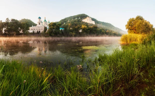 Beautiful morning sunrise with fog on the water. Temple on the river bank at sunrise, reflected in the river. Temple on chalk cliffs at dawn, over the river. Traditional ukrainian landscape.