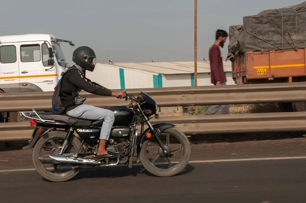 Morbi, Gujarat, India - 12 02 2022: A young man in a helmet rides a motorcycle on an Indian road.