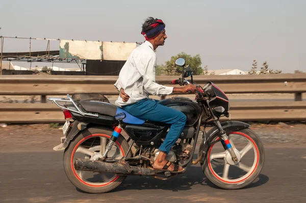 Morbi, Gujarat, India - 12 02 2022: A man without helmet rides motorbike along indian road. Out of the city.