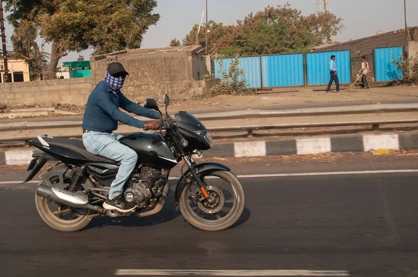 A young man without helmet rides a motorcycle on an Indian road.