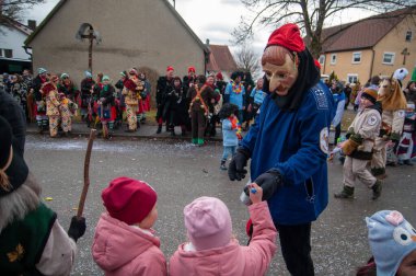 Hohenstadt - February 17, 2023: Participants of a parade with traditional costumes and masks at the carnival parade in Hohenstadt, Germany. Distribute sweets to children