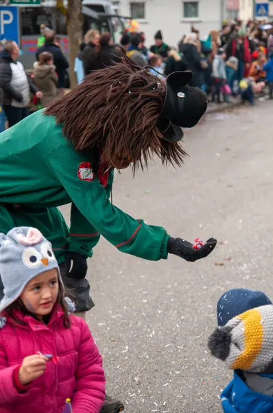 Hohenstadt - February 17, 2023: Participants of a parade with traditional costumes and masks at the carnival parade in Hohenstadt, Germany. Distribute sweets to children