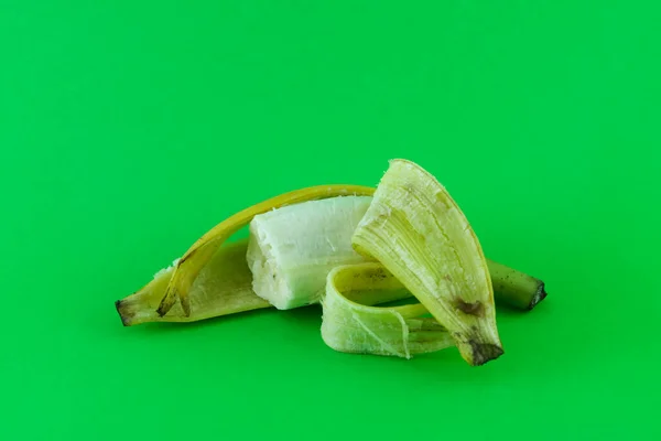 close up of a ripe banana. the fruit is eaten, the skin peels off. Banana peel is greenish yellow. against a plain green background.
