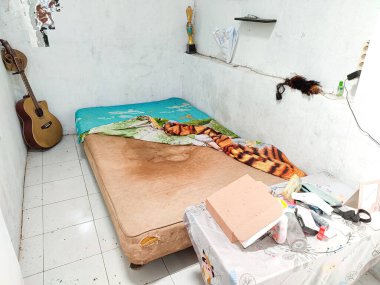 Klaten, Indonesia - December 2022 : the room atmosphere is untidy and dirty. a bed to lie down to unwind in the house. messy home interior real life. white floor and white walls.