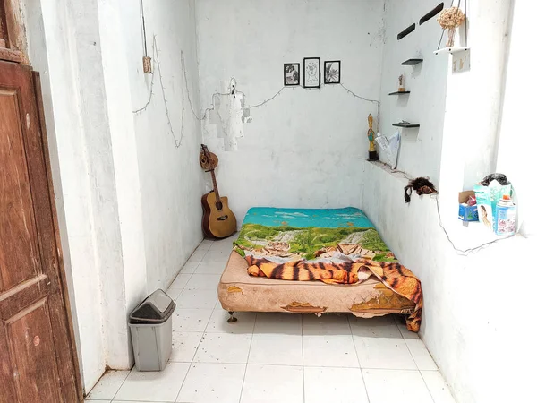 Klaten, Indonesia - December 2022 : the room atmosphere is untidy and dirty. a bed to lie down to unwind in the house. messy home interior real life. white floor and white walls.