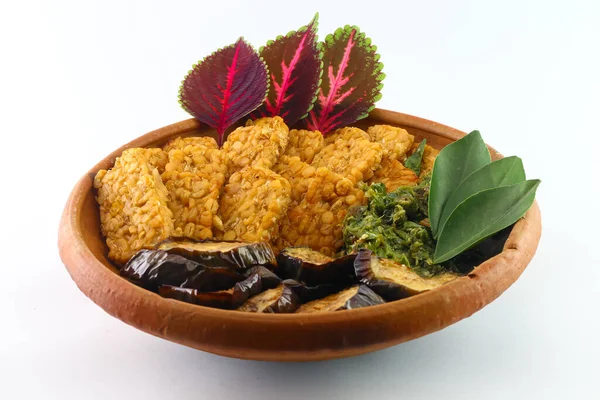 Mendoan veya kızarmış tempeh. Kızarmış soya fasulyesi. Kolesterol gıdaları. Kızarmış patlıcan ve yeşil biberleri birleştirin. Kil tabakta servis edilir. düz beyaz bir arkaplanda.