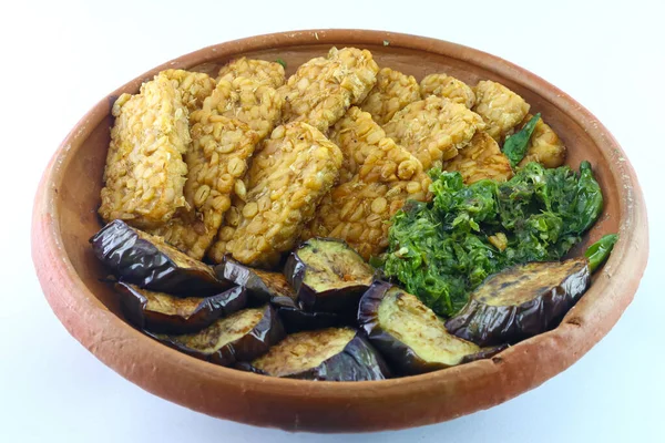 Mendoan veya kızarmış tempeh. Kızarmış soya fasulyesi. Kolesterol gıdaları. Kızarmış patlıcan ve yeşil biberleri birleştirin. Kil tabakta servis edilir. düz beyaz bir arkaplanda.