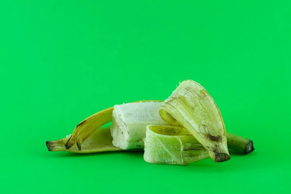 close up of a ripe banana. the fruit is eaten, the skin peels off. Banana peel is greenish yellow. against a plain green background.