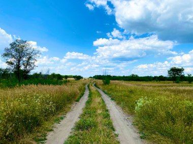 Uncovered country road overgrown with grass and the sky is very blue
