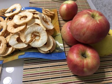 Fresh apples on the kitchen table next to fresh apple chips on a blue square plate.
