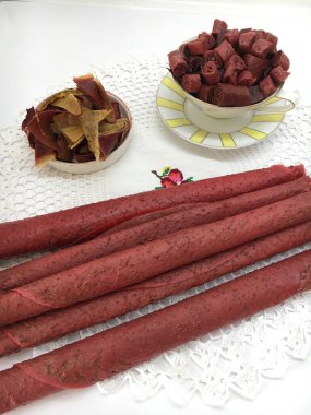 Red pastila in straws and sliced fruit pastille on a saucer and in a cup against the background of a lace napkin.