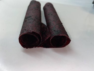 Siyah frenk üzümünden yapılmış meyveli pastil beyaz bir masada bir tüpe sarılmış..