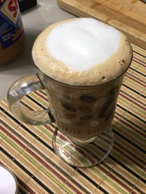 Cup of cappuccino coffee with a handle on a white table on a bamboo mat close-up