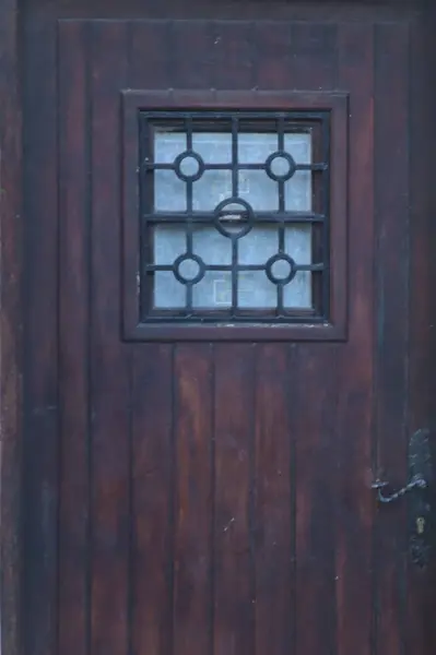 main door of a strong wooden farmhouse with a small glass window and iron grill