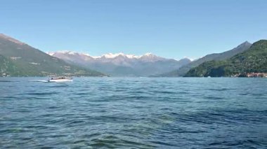 İtalya 'daki Como gölünün arka planında karlı dağlar ve turistlerle dolu bir motorlu tekne sahnesi.