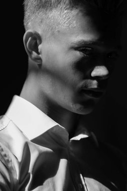 Düşen ışıkla birlikte karanlık arka planda duran bir adamın siyah beyaz portresi. 