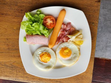 Beyaz bir tabağa konmuş yumurta, sosis ve sebzelerden oluşan kahvaltı seti..