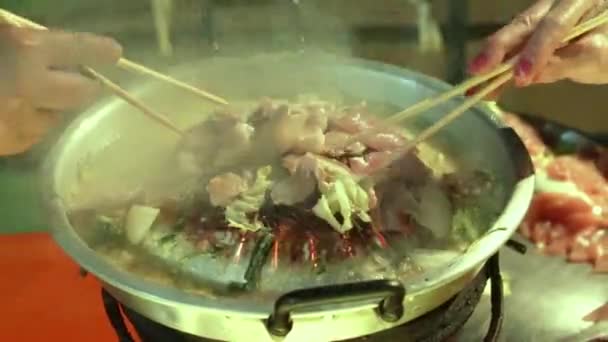 两个男人和女人用绞刑架把猪肉烤在锅里 不停地翻动 直到烤好为止 — 图库视频影像