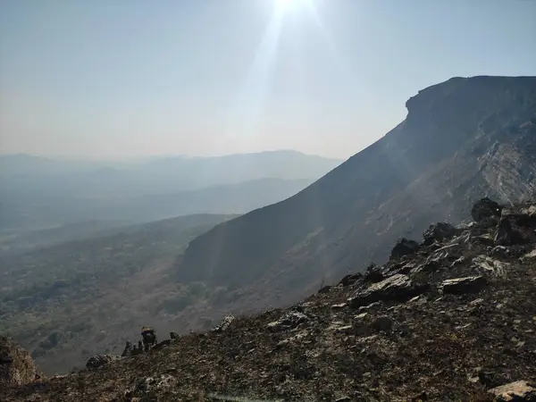Gökyüzüne karşı yükselen tepeyi aydınlatan güneş ışığıyla görkemli bir dağ manzarası..