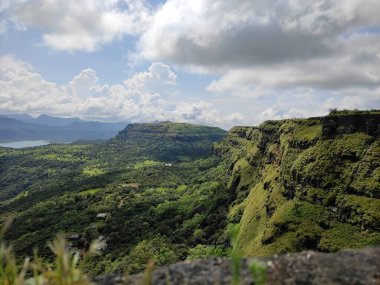 Resim dalgalanan tepelerin arasına gizlenmiş yemyeşil bir vadiyi güzel bir şekilde tasvir ediyor. Tarlalar ve yemyeşil ağaçlar bölgeyi güzelleştiriyor. Resim, gökyüzünü kaplayan bulutlardan derinlik ve zenginlik kazanıyor..