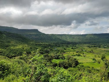 Görüntü, gökyüzünün bulutlarla, arazinin yeşilliklerle ve kır çiçekleriyle dolu olduğu dağlık bir manzaranın nefes kesici görüntüsünü yakalıyor. Görüntüdeki renkler canlı, gökyüzünün mavisi ile. Genel olarak.