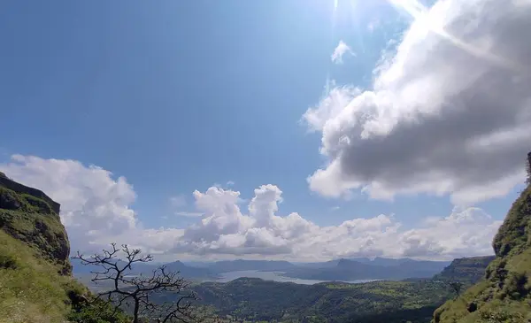 Berrak mavi gökyüzü altında nefes kesen dağ manzarası, çeşitli bitki örtüsü ve dingin su, parlak güneş ışığıyla aydınlanıyor..