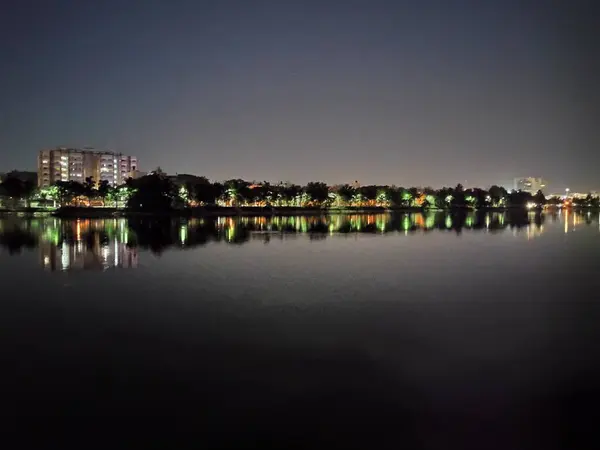 Huzurlu gece sahnesi, şehrin uzak ışıklarını yansıtan büyük bir su kütlesini yakalar. Sakin su, huzurlu bir ortam yaratıyor ve manzaranın güzelliğini arttırıyor..