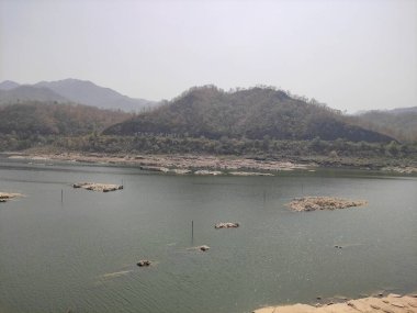 Dağlar ve berrak gökyüzü ile çevrili olan resimde geniş bir su kütlesi görülüyor..