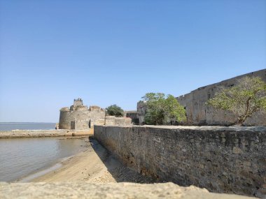 The picture depicts a calm lakeside setting along the shore, complete with a Diu Fortress. clipart