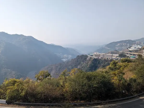 Virajlı bir yolu ve uzakta büyük bir binası olan dağlık bir bölgenin manzarası..