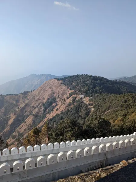 Resim, taştan bir duvarı ve dolambaçlı bir yolu olan bir dağ sırasının huzurlu bir görüntüsünü gösteriyor..