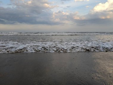 Görüntü sakin bir sahneyi yakalıyor dalgalar yavaşça kıyıya vuruyor sisli bir gökyüzünün altında.