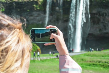 Iceland - 06.03.2019: Woman in Light Pink Coat Take a Photo of Waterfall, Iceland