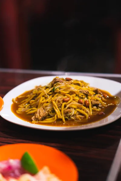 stock image Mie Aceh is spicy noodle cuisine in Indonesia. Yellow noodles cooked with spices, herb, squid and has curry taste. Served with fried nut, shallot pickles. Focus selection and blurry selection.