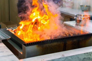 Şefin ellerini mangalda sosis şiş pişirirken, karides ve sebzeler ızgarada cızırdarken yakın çekim. Ateşle