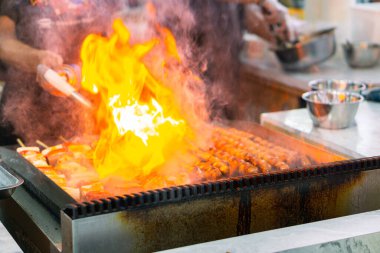 Şefin ellerini mangalda sosis şiş pişirirken, karides ve sebzeler ızgarada cızırdarken yakın çekim. Ateşle