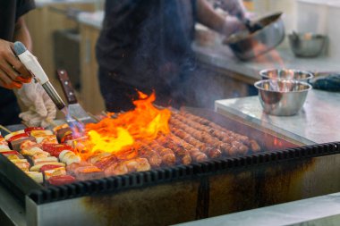 Şefin ellerini mangalda sosis şiş pişirirken, karides ve sebzeler ızgarada cızırdarken yakın çekim. Ateşle