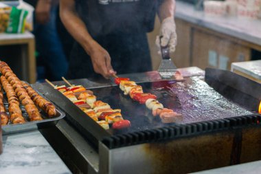 Bir şefin ellerini mangalda sosis şişi pişirirken yakın çekim.