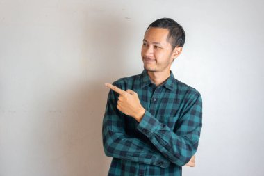 Genç Yetişkin Asyalı erkekler, gülümseyen yüzleriyle parmağını sola doğru uzatıyor ve dışlanmış beyaz arka planlı ifadeden çıkıyorlar.