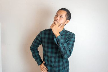 Genç, sakallı, yeşil flanel gömlek giyen Asyalı adam düşünme hareketi gösteriyor. Çene üzerinde kalça