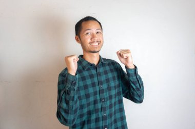 Aşırı neşeli beyaz arka planda Asyalı genç adamlar yumruklarını sıkarak başarıyı kutluyorlar.