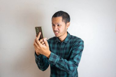 Yeşil flanel giyen genç adamlar, izole edilmiş beyaz arka planda akıllı telefon okurken kızgınlar.