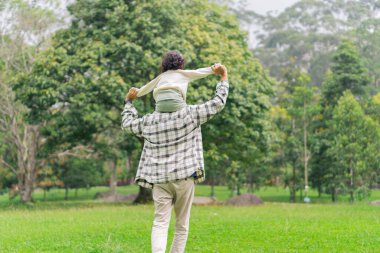 Baba ve kızının park bahçesinde sırt sırta koşarkenki görüntüsü.